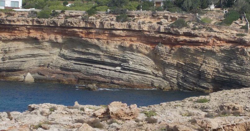 De rotsige westkust bij Cala Codolar op Ibiza — geologische lagen en kristalhelder water