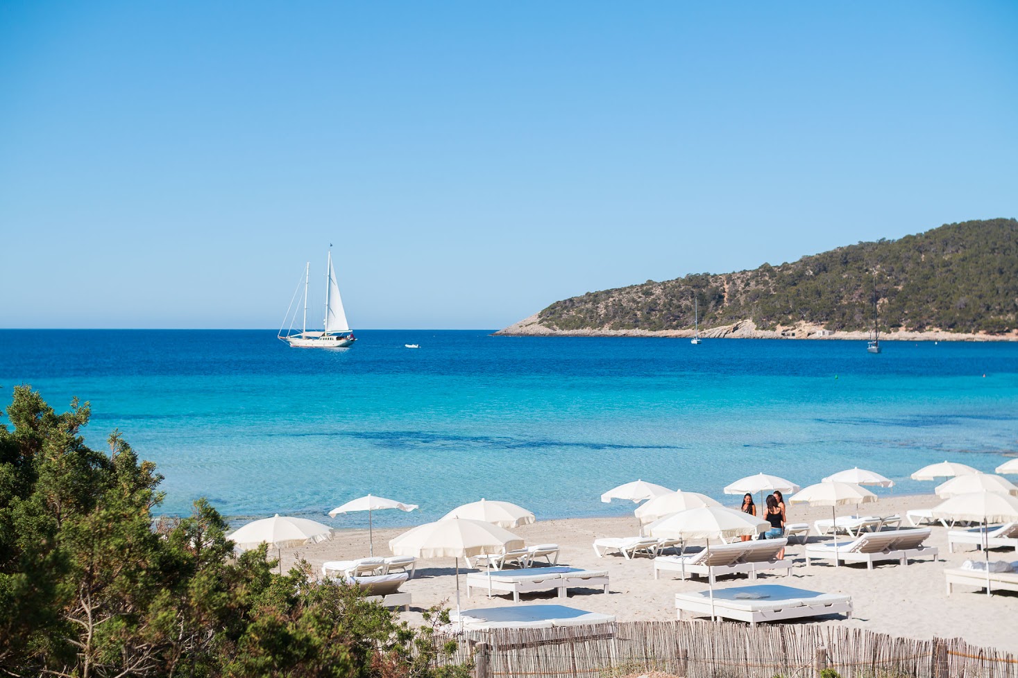 Witte parasols van Jockey Club met zeilboot in baai