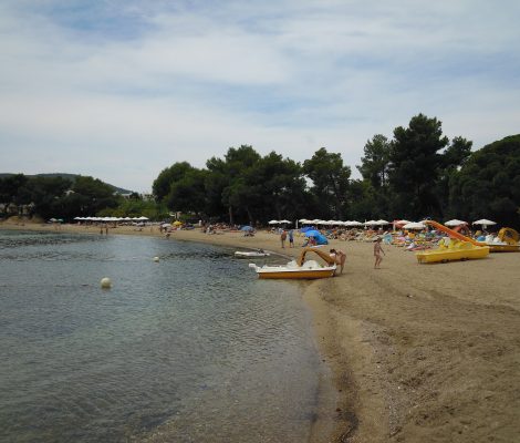 Het strand van Niu Blau op Ibiza — gouden zand, pijnbomen op de achtergrond en gele pedalo's klaar voor verhuur