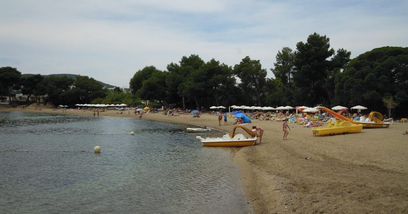Het strand van Niu Blau op Ibiza — gouden zand, pijnbomen op de achtergrond en gele pedalo's klaar voor verhuur