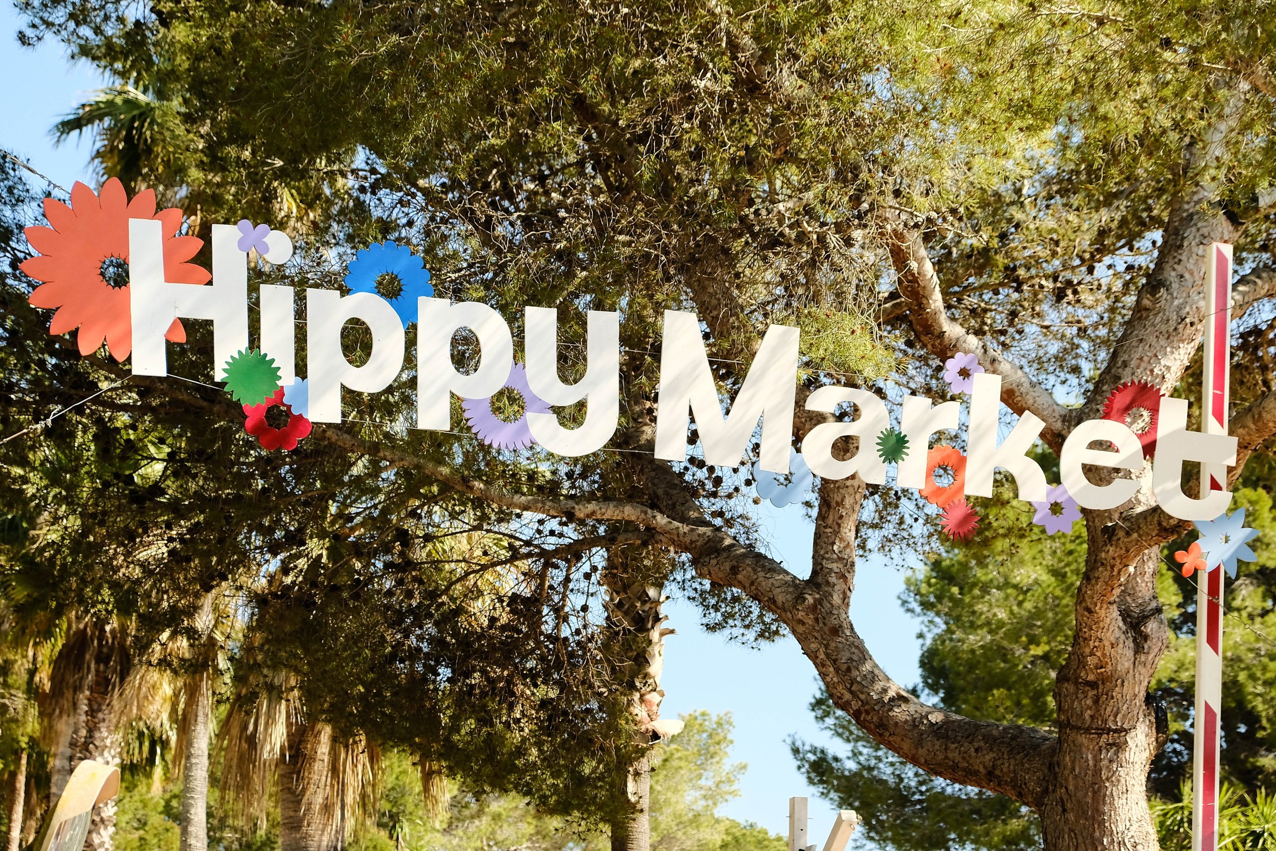Het Hippy Market-bord met bloemen tussen pijnbomen bij Punta Arabí