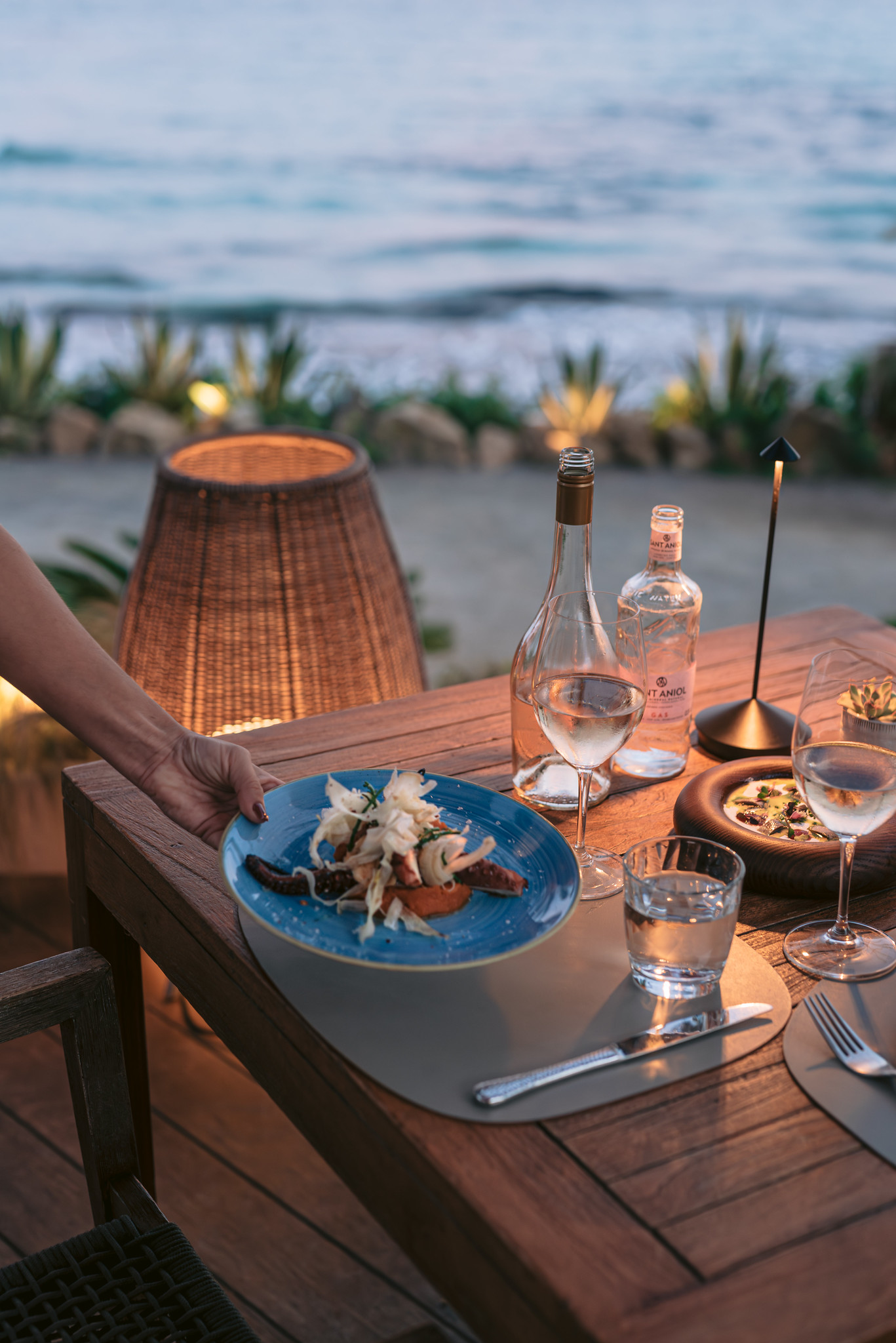 Aiyanna Ibiza: strandrestaurant met Levantijnse keuken aan Cala Nova 3 Een bord met octopus en venkel bij Aiyanna aan Cala Nova bij schemer, met een glas rose en de zee op de achtergrond, Ibiza