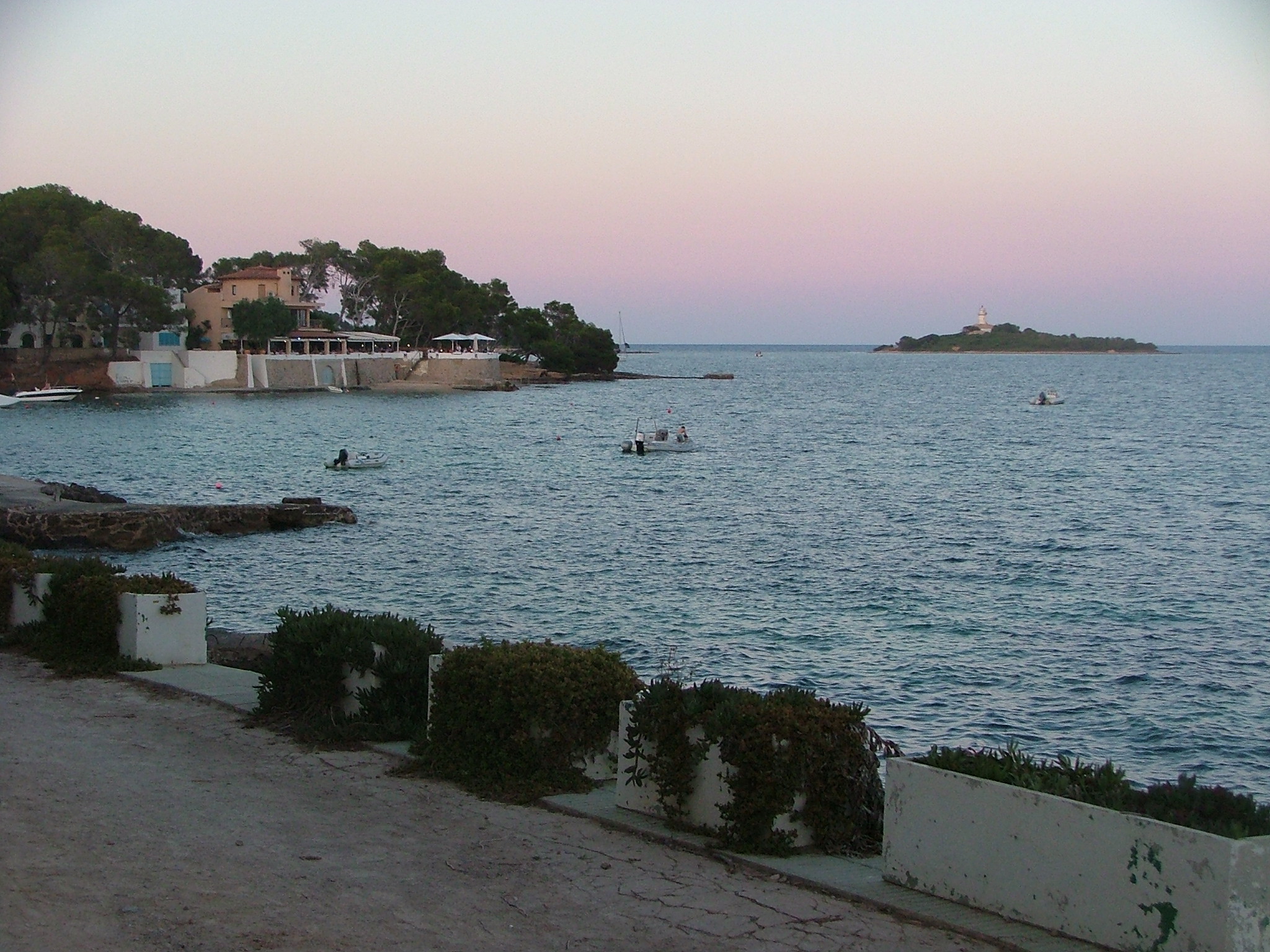 Alcanada Mallorca: rustig snorkelstrand met vuurtoreneilandje 2 De baai van Alcanada bij Alcúdia in het avondlicht, met villa's tussen de pijnbomen, bootjes en het vuurtoreneilandje in de verte, Mallorca