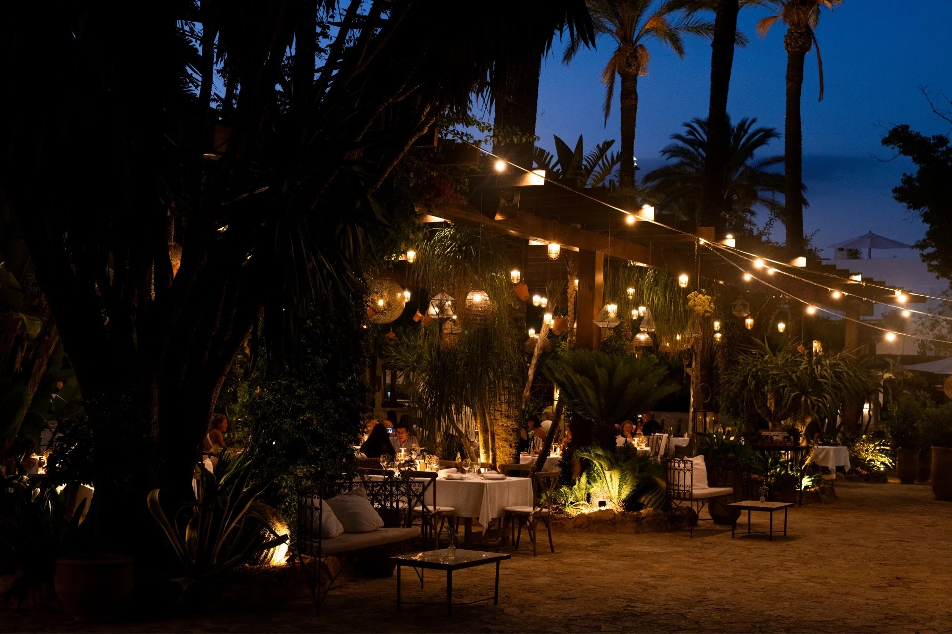 Het tuinrestaurant van Atzaró bij schemer, met lantaarns, lichtslingers en gedekte tafels tussen de palmen