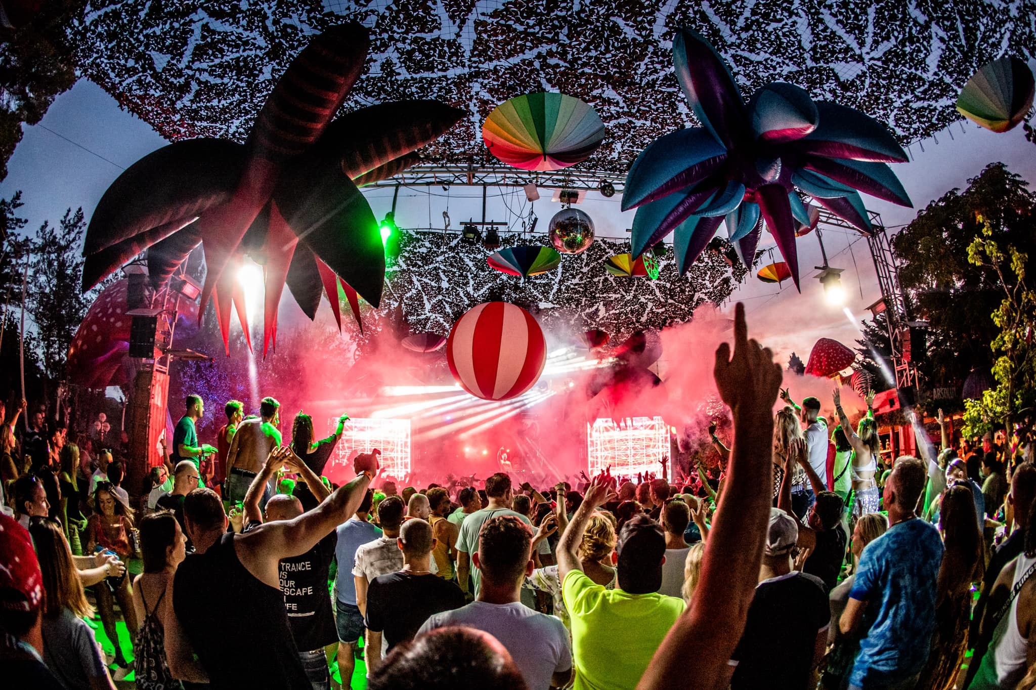 De open-air dansvloer van Benimussa Park op Ibiza tijdens The Zoo Project, met opblaaspalmen, discobal en dansende menigte