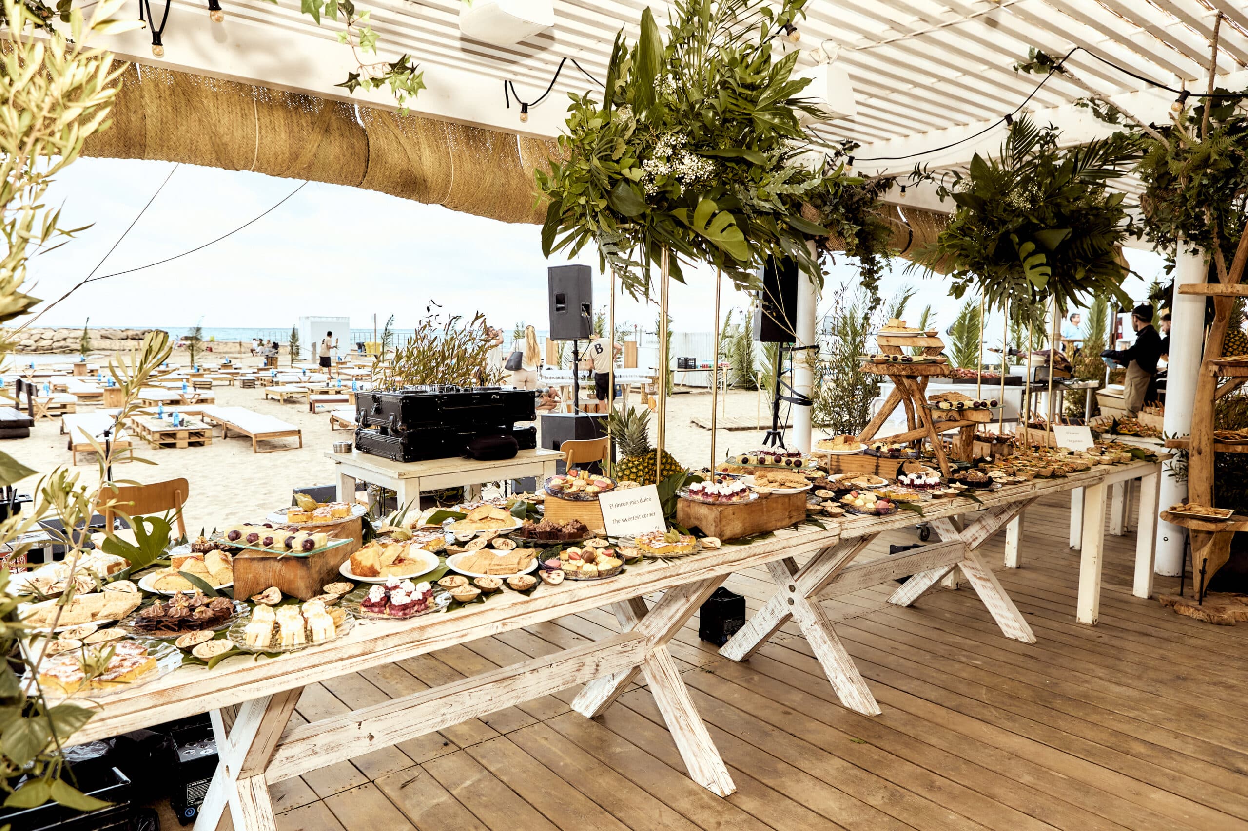 Een royale foodspread op een lange tafel onder de pergola van Beso Beach aan Ses Salines, met het strand en de zee op de achtergrond, Ibiza