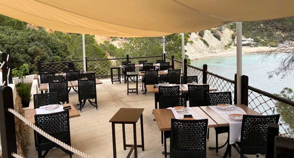 Het terras van Es Boldado onder crèmekleurige zonnezeilen met uitzicht over de baai van Cala d'Hort, Ibiza