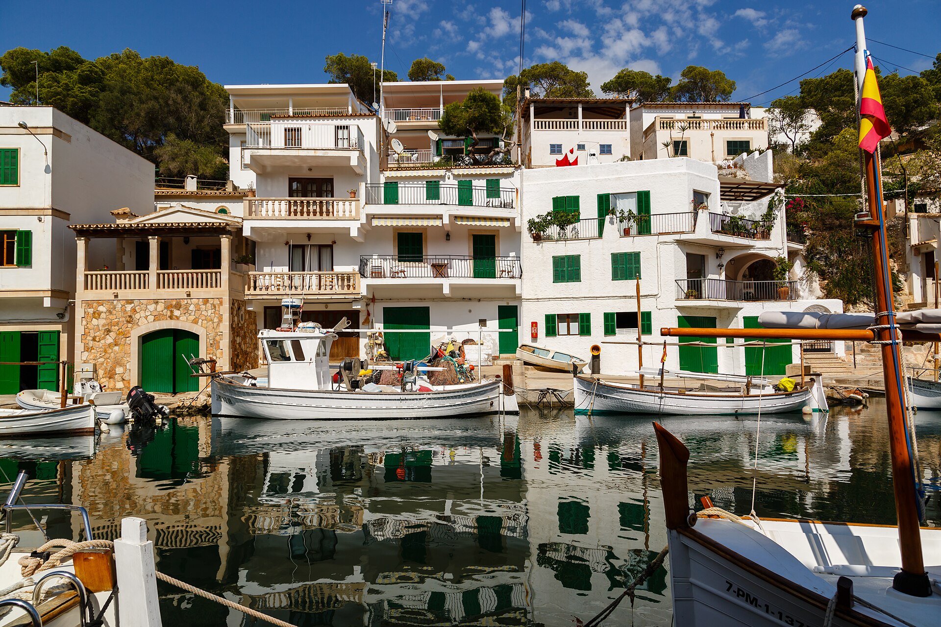 Witte vissershuizen met groene luiken en traditionele boten in het spiegelende water van het haventje van Cala Figuera, Mallorca