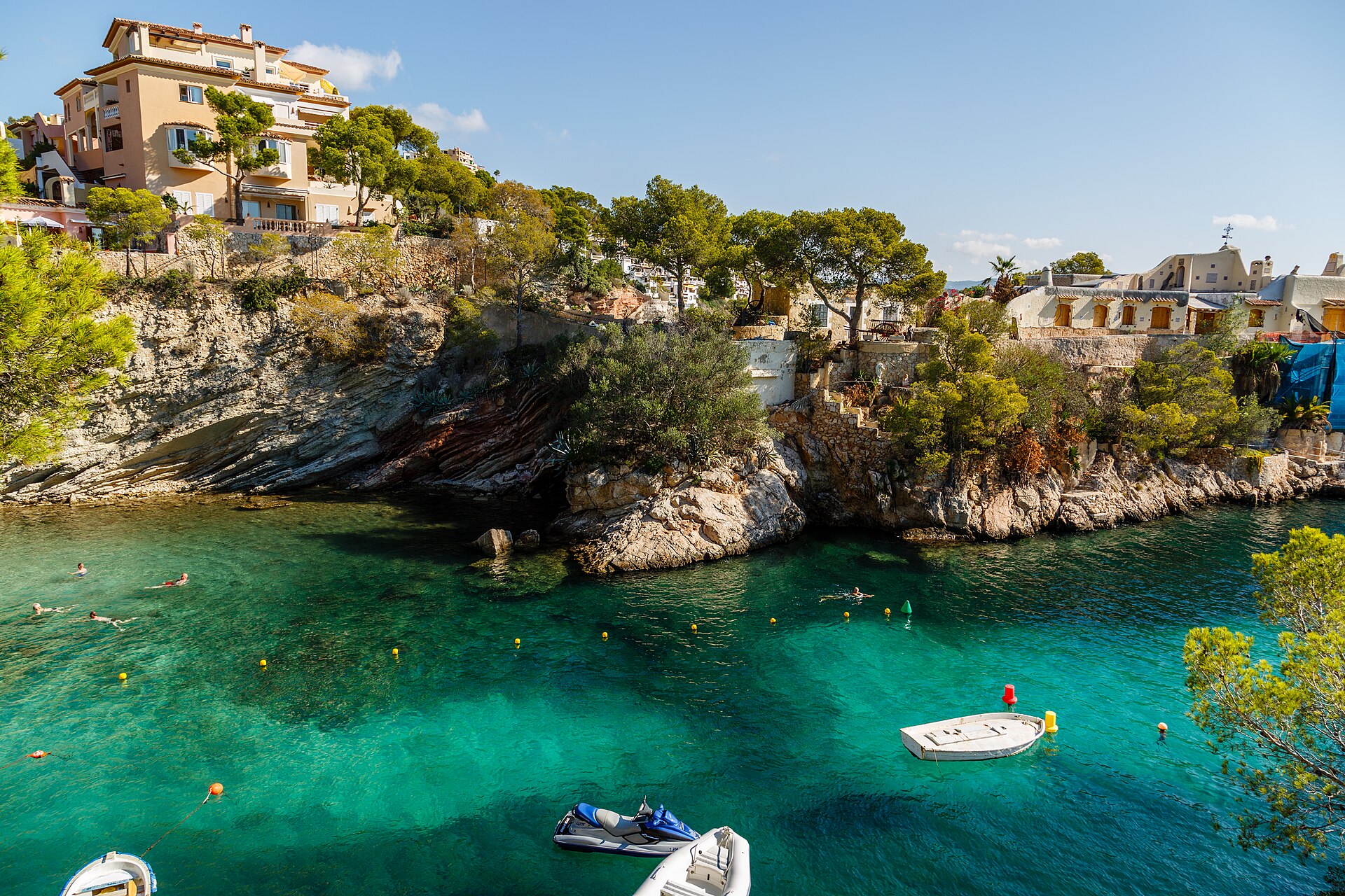 Kristalhelder turquoise water in een rotsige baai van Cala Fornells met okerkleurige villa's tussen de pijnbomen, Mallorca