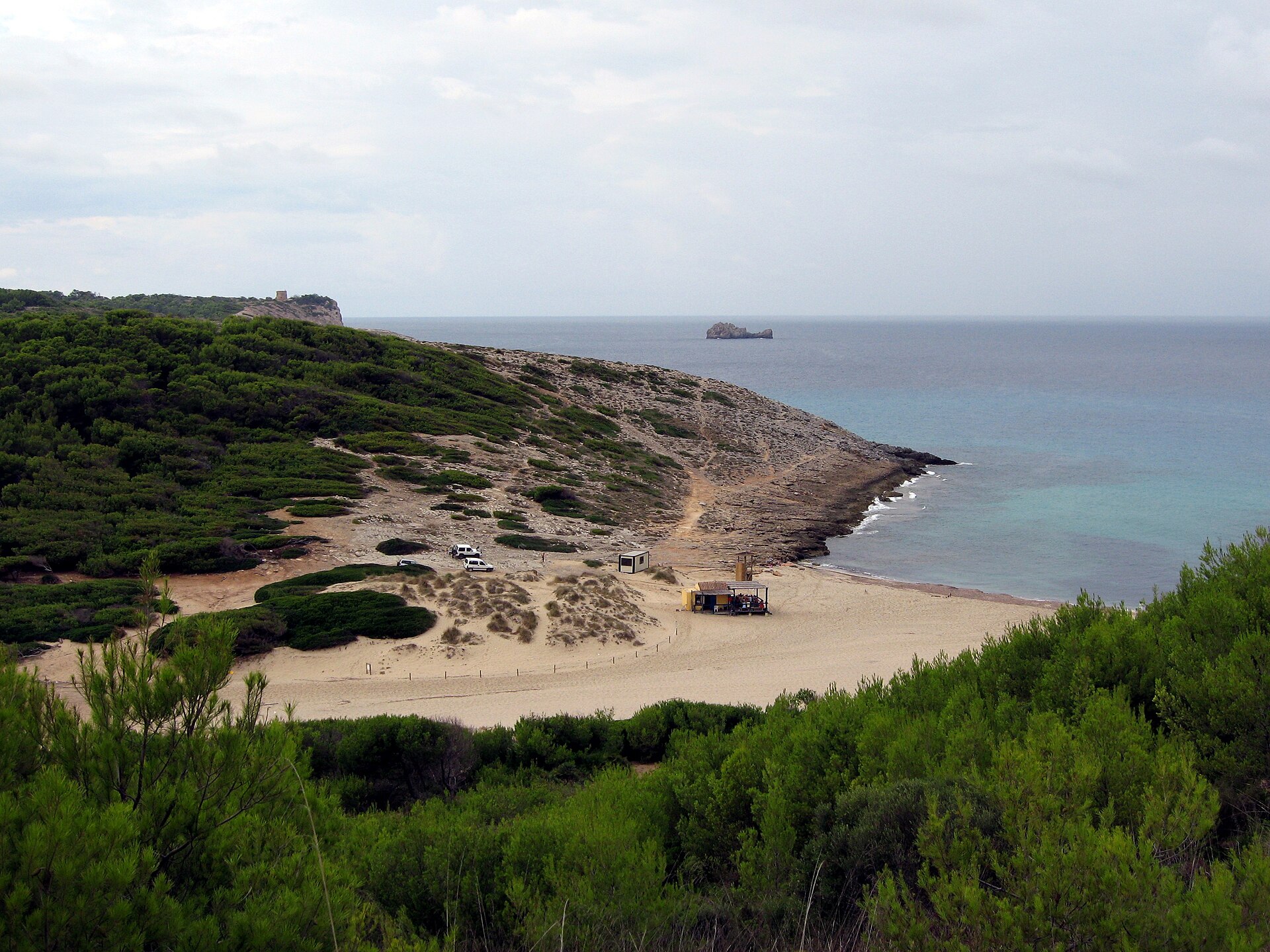 Overzicht van de duinen en de baai van Cala Torta met een oude wachttoren op de kaap en een klein strandbarretje