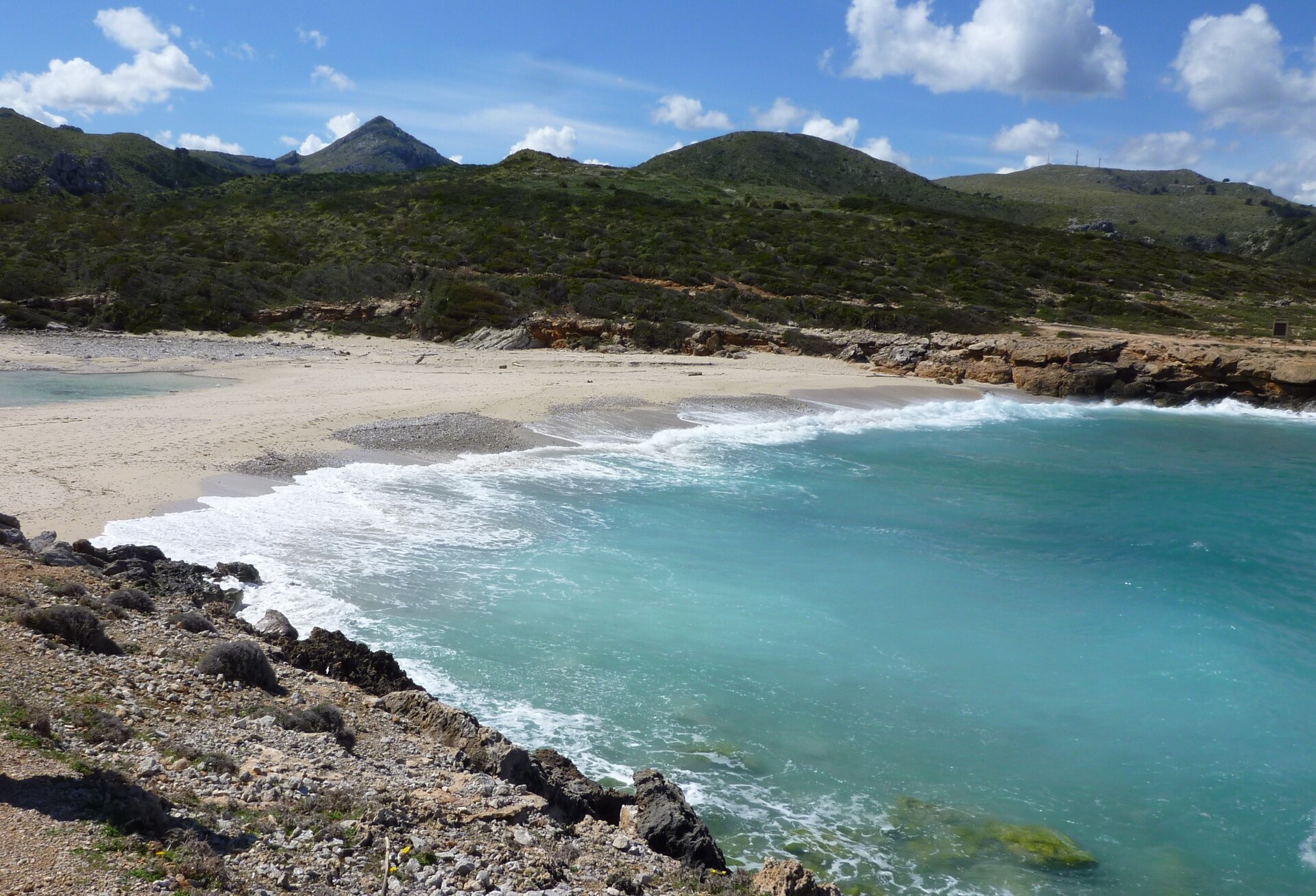 Het wilde, lege strand van Cala Torta met turquoise water en groene heuvels in het noordoosten van Mallorca
