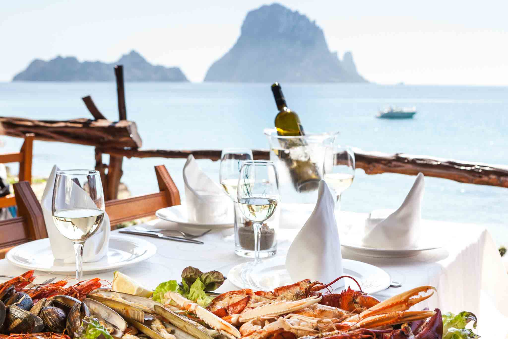 Een gedekte tafel met een grote zeevruchtenschotel op het terras van El Carmen aan Cala d'Hort, met de rots Es Vedrà op de achtergrond, Ibiza