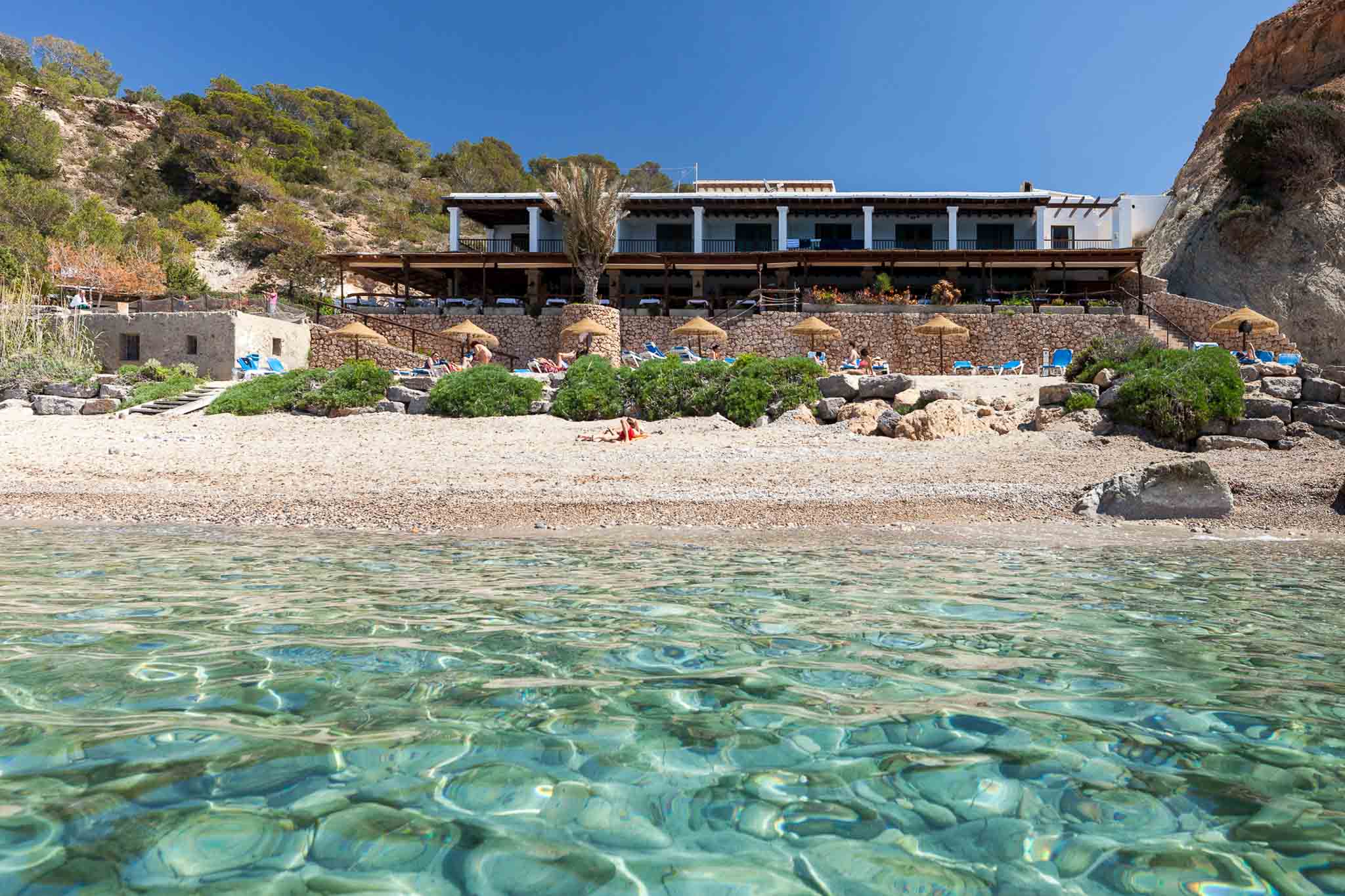 Het witte restaurant El Carmen op het strand van Cala d'Hort, gezien vanaf het heldere turquoise water, Ibiza