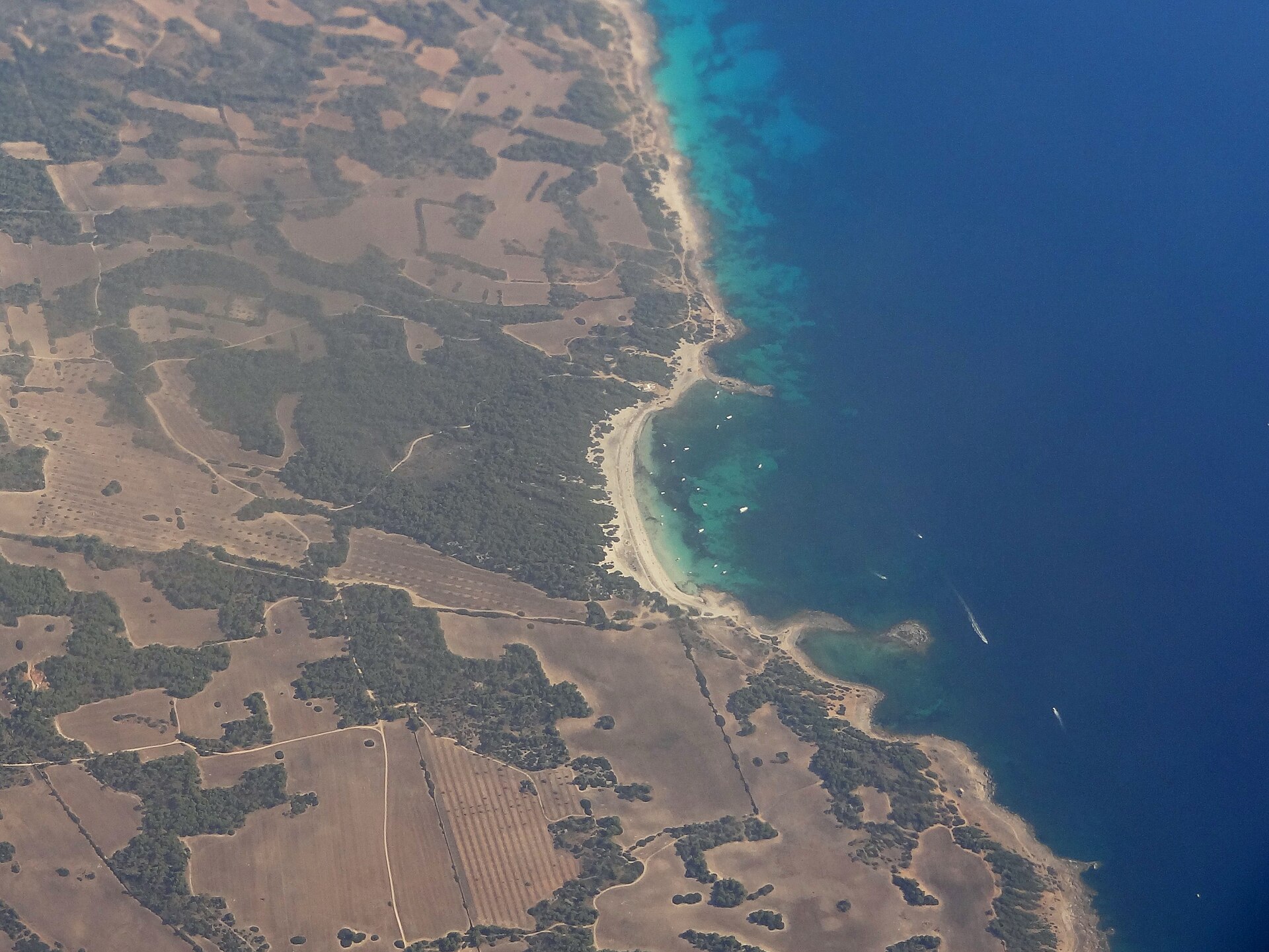 Luchtfoto van de zuidkust van Mallorca met de witte zandboog van Es Caragol, turquoise water en ankerende boten tussen droog boerenland