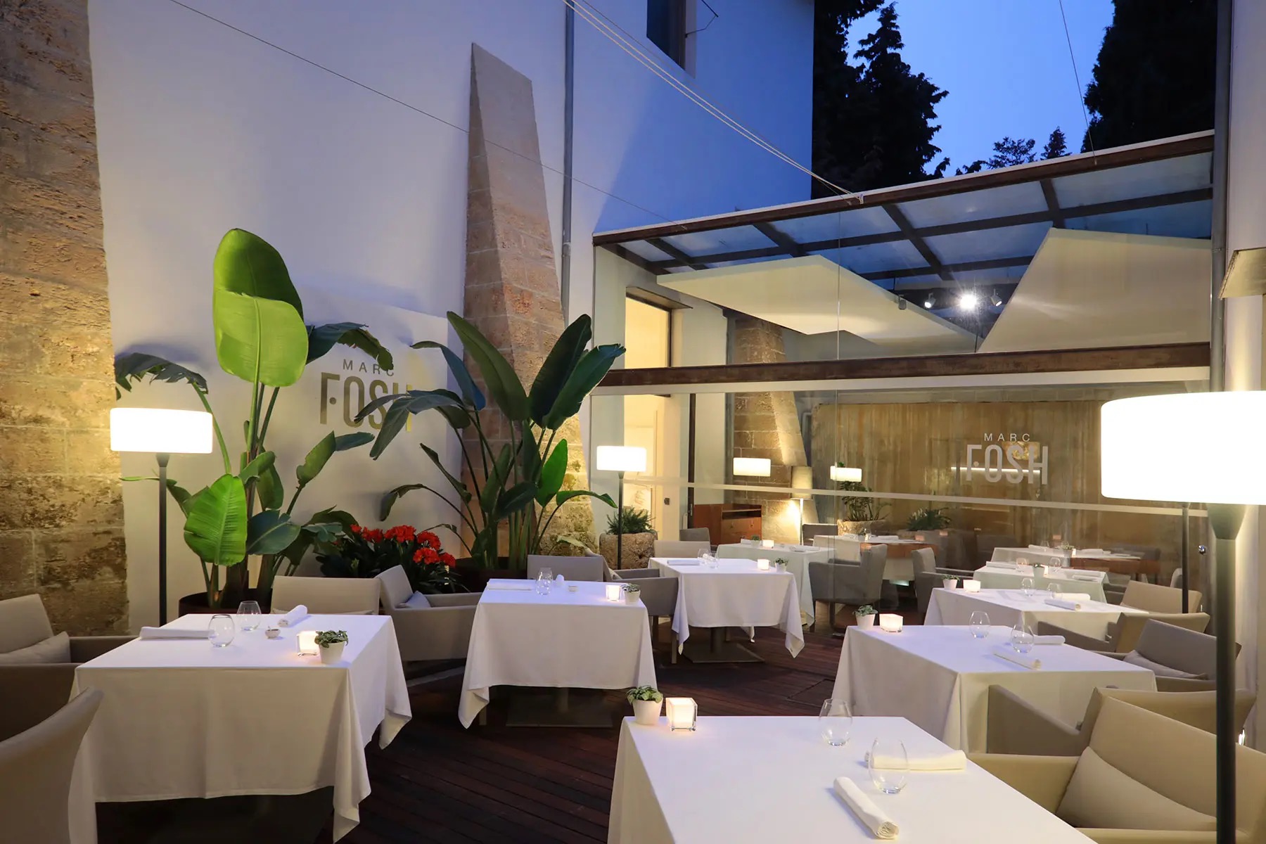 Het sfeervolle binnenplaatsterras van restaurant Marc Fosh bij schemer, met gedekte tafels en de kloostermuren, Palma, Mallorca
