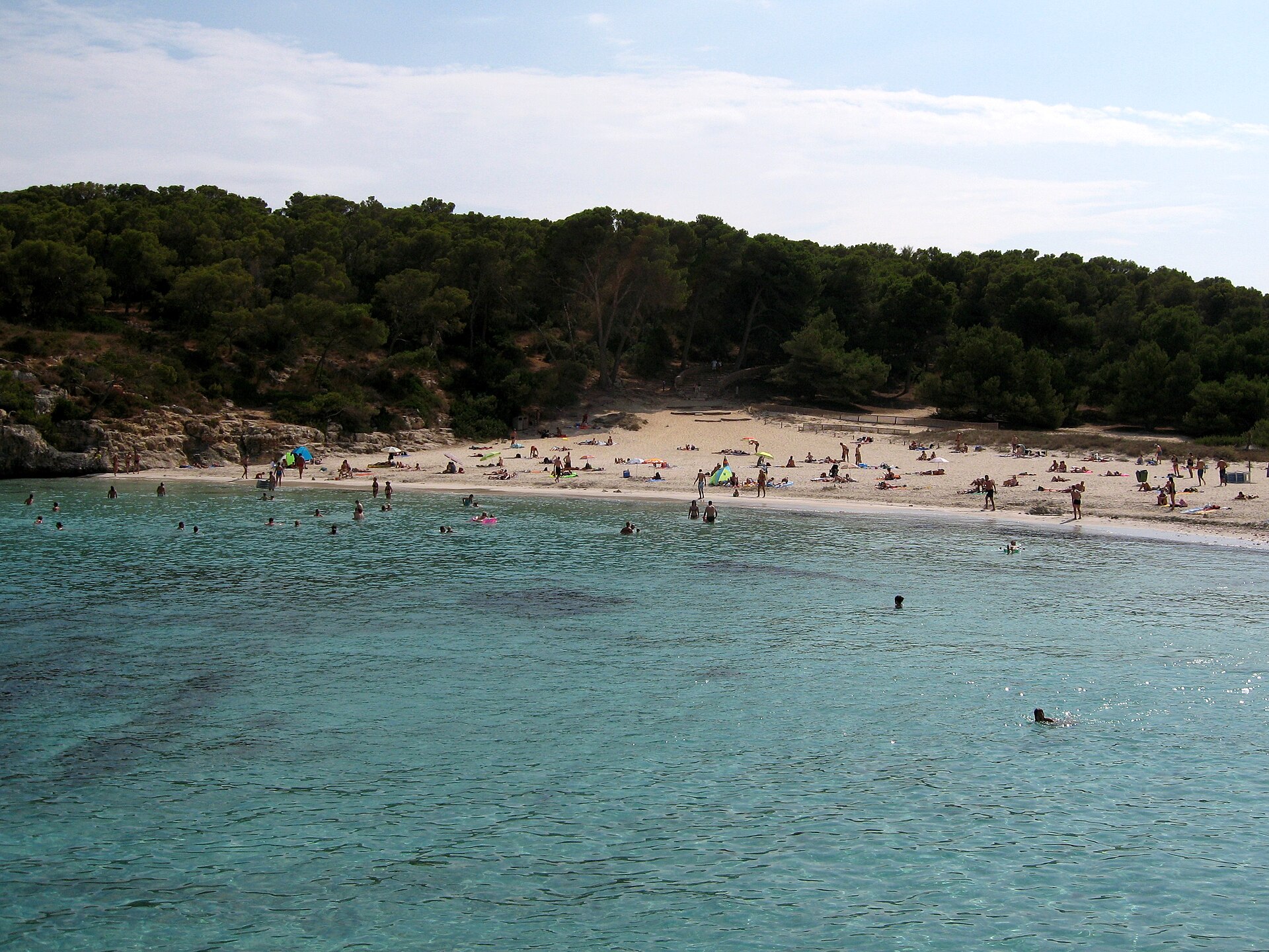 Het witte strand van S'Amarador met helder turquoise water, badgasten en een pijnbos op de achtergrond, Mallorca