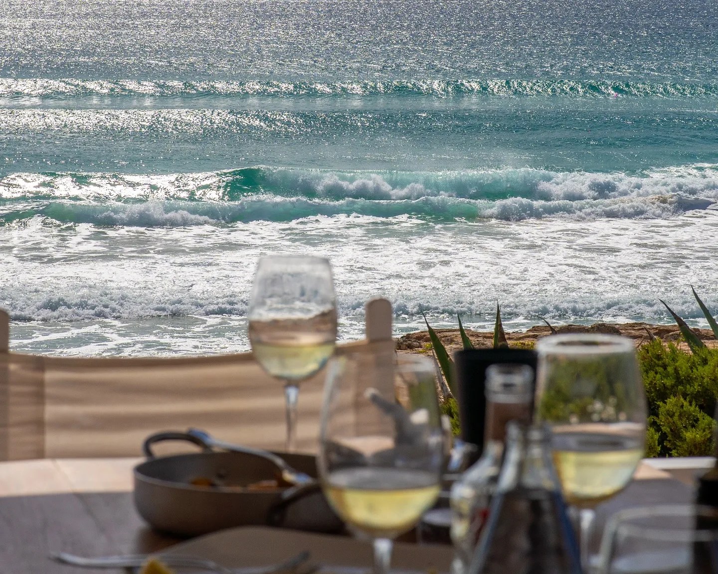 10.7 Formentera: zonsondergang en fusionkeuken aan Platja de Migjorn 7 Glazen witte wijn op tafel met de zee op de achtergrond bij 10.7