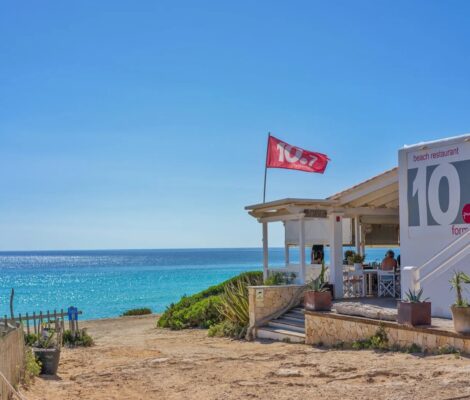 De witte strandlounge 10.7 met de vlag boven Platja de Migjorn en de turquoise zee