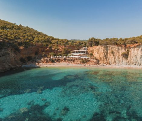 De turquoise baai van Sol d'en Serra met het kiezelstrand en restaurant Amante op de rode klif tussen de pijnbomen