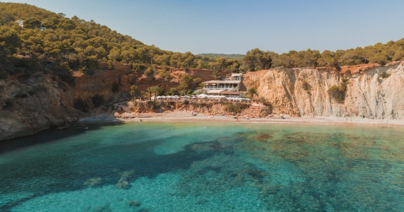 De turquoise baai van Sol d'en Serra met het kiezelstrand en restaurant Amante op de rode klif tussen de pijnbomen