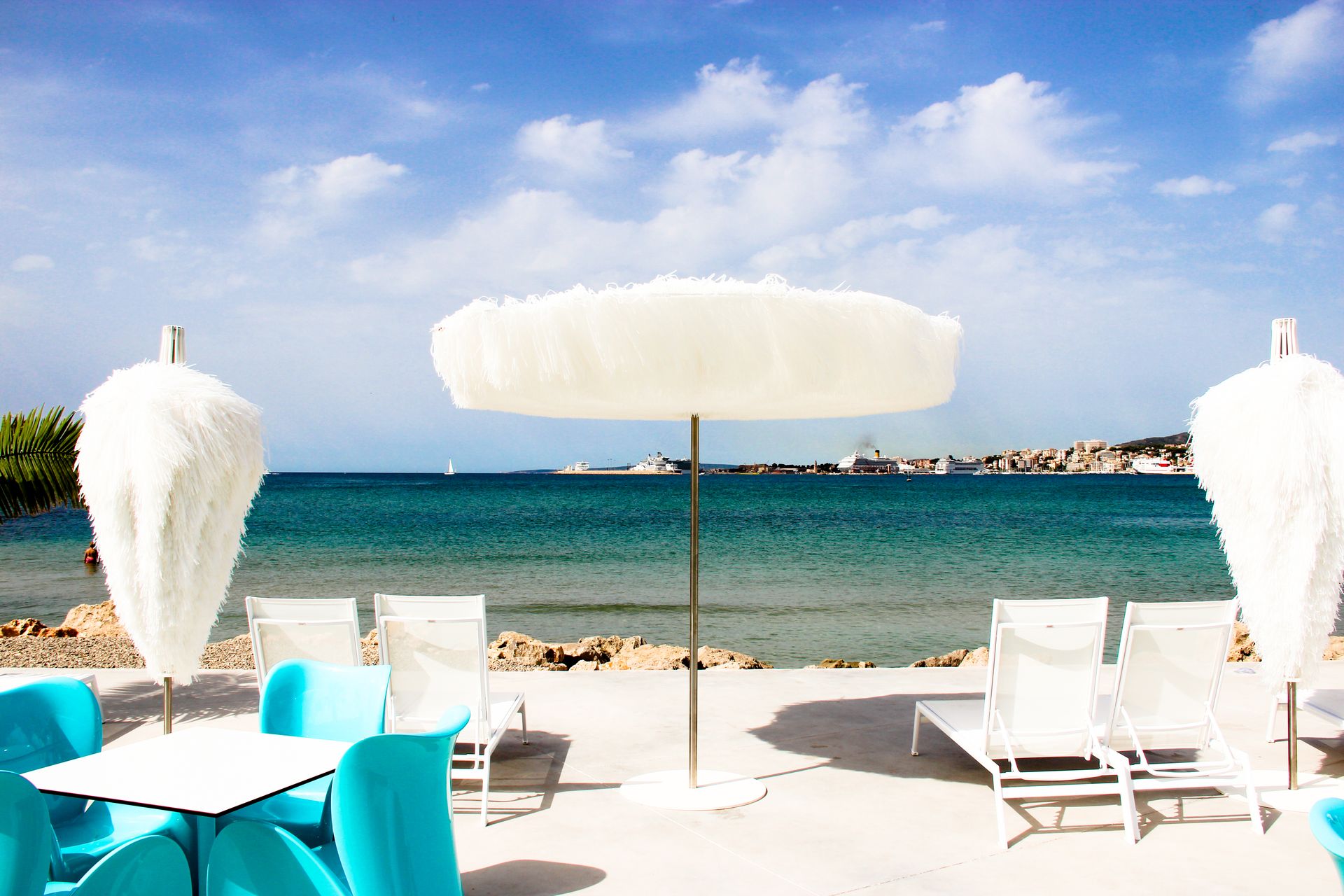 Anima Beach Mallorca: beachclub aan het stadstrand van Palma 2 Witte parasol, ligstoelen en tafel van Anima Beach met uitzicht over de Baai van Palma