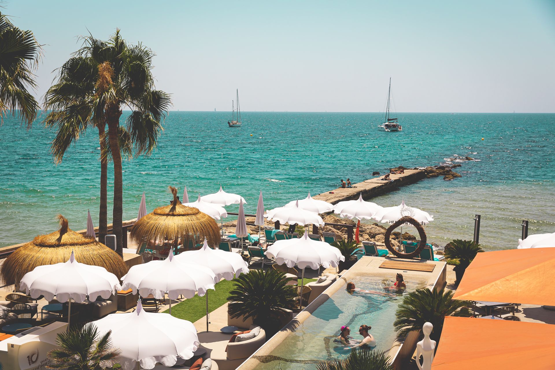Anima Beach Mallorca: beachclub aan het stadstrand van Palma 1 Het zwembad en de parasols van Anima Beach met de Baai van Palma en de pier erachter