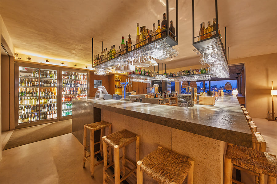 Assaona Portixol (Palma): gastrobeachclub op het zand, het hele jaar open 3 De bar van Assaona met een stenen toog en een verlichte flessenwand