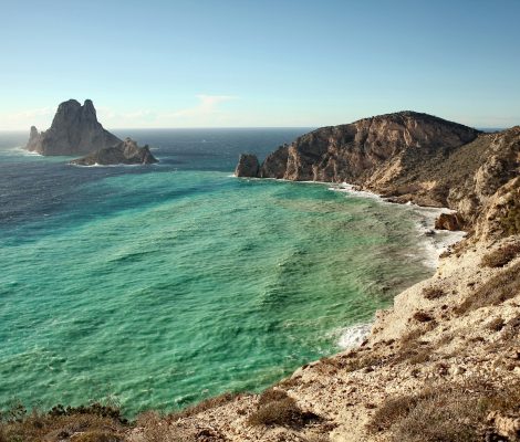 Turquoise zee in de baai onder Sa Pedrera met de kliffen van de zuidwestkust en de rotseilanden Es Vedrà en Es Vedranell op de achtergrond