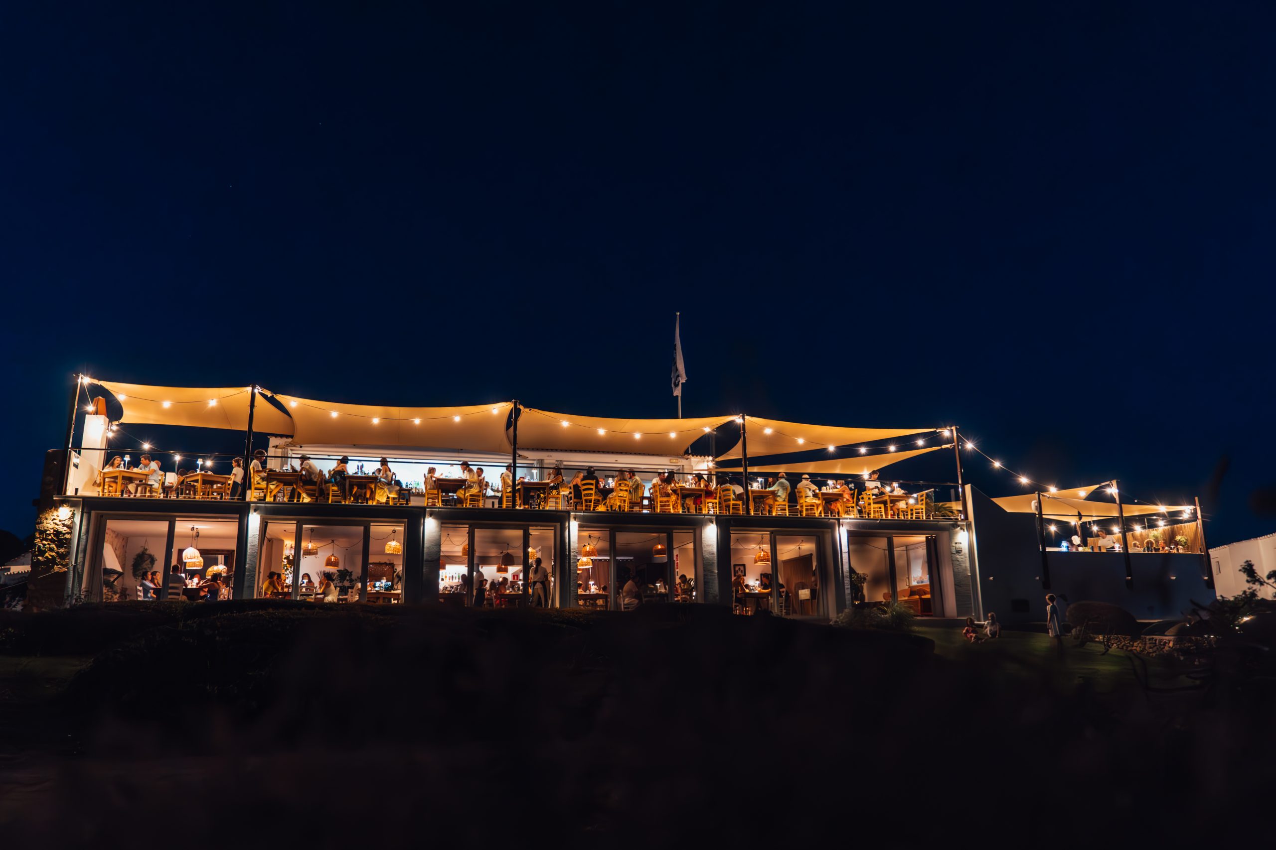 Bambú Menorca 's avonds verlicht, met de twee niveaus boven de donkere kust