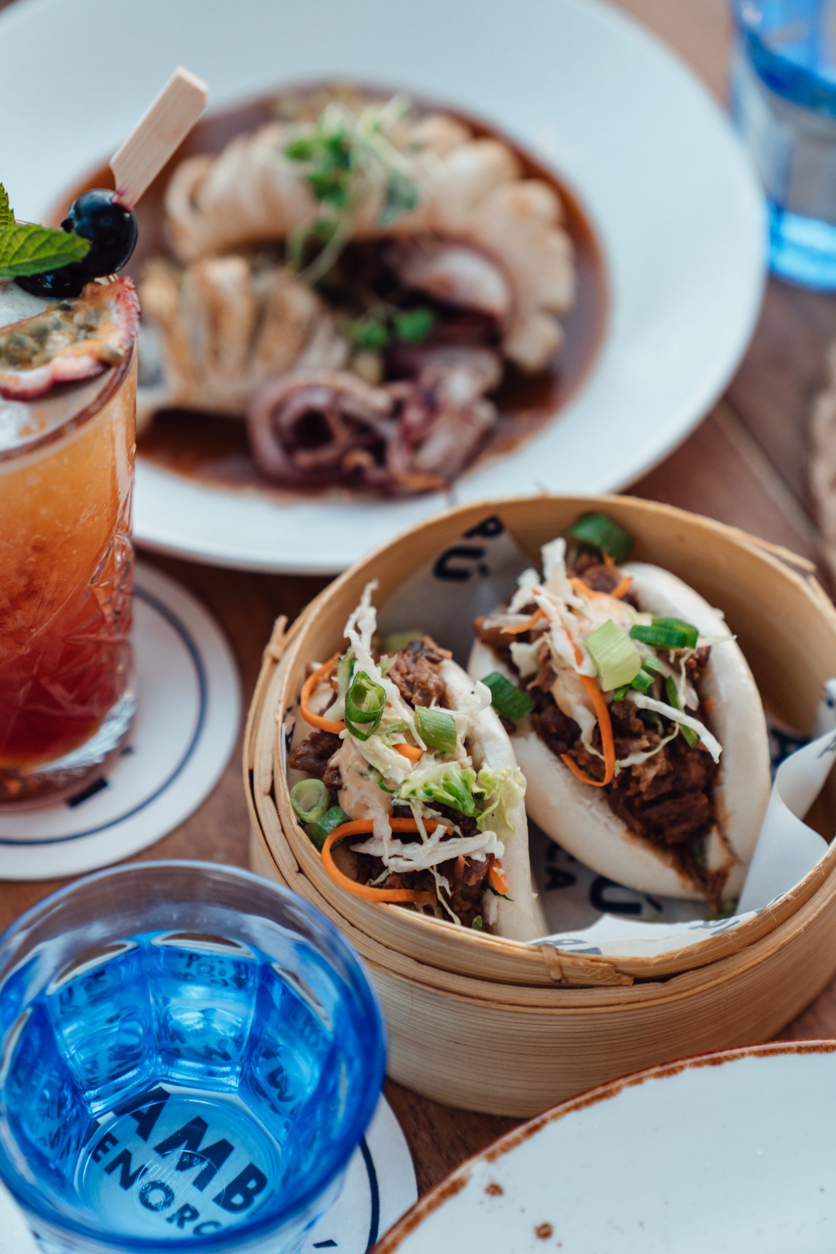 Bao buns in een bamboestomer met een blauw glas bij Bambú Menorca