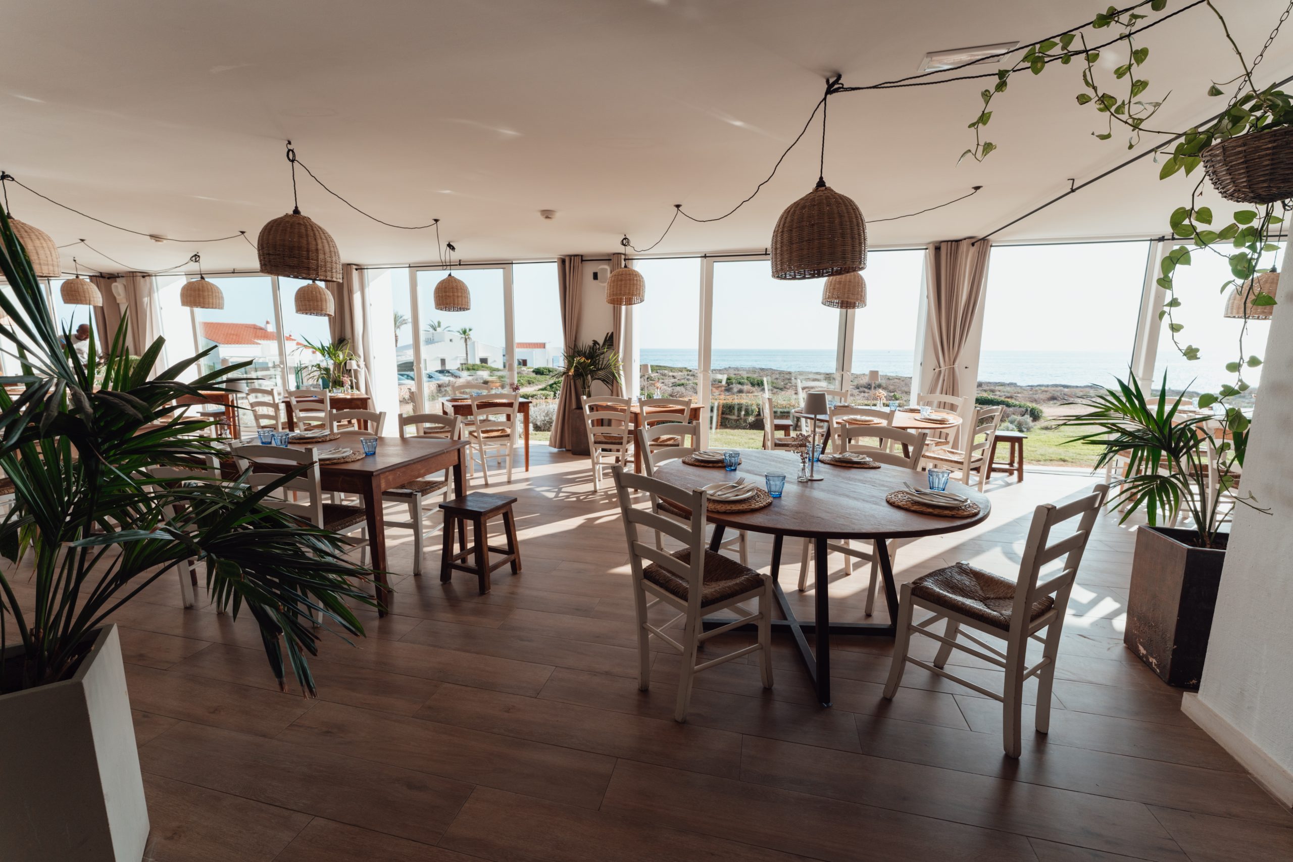 De lichte eetzaal van Bambú Menorca met rieten hanglampen, planten en zeezicht