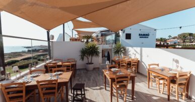 Het terras met gedekte tafels van Bambú Menorca onder zonnezeilen met de zee erachter