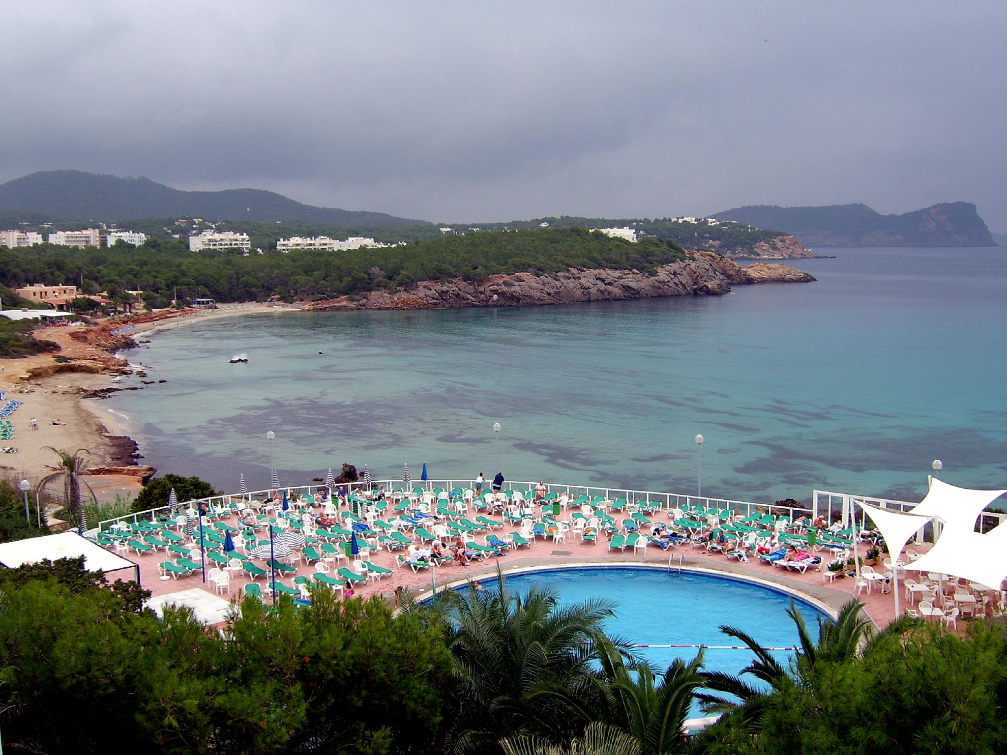 Beachclubs op Ibiza: waar ze zitten, seizoen en reserveren 7 De baai van Cala Nova bij Sant Carles op Ibiza met parasols op het zand en beboste heuvels rondom