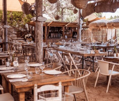 Het rustieke terras met houten tafels onder het rieten dak van Beso Beach op Ses Illetes, Formentera