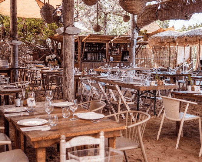 Het rustieke terras met houten tafels onder het rieten dak van Beso Beach op Ses Illetes, Formentera
