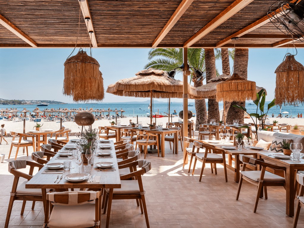 Beso Beach Palmanova (Mallorca): barefoot-luxury aan het strand 4 Gedekte tafels van Beso Beach Mallorca met parasols en de zee op de achtergrond