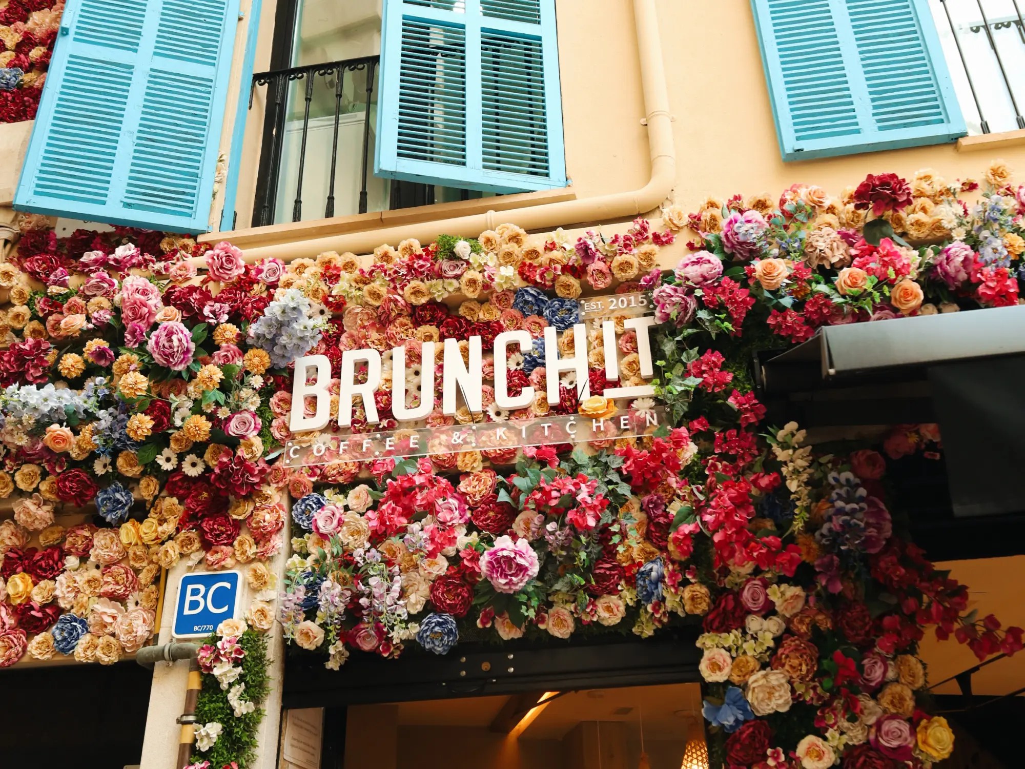 De met bloemen bedekte gevel van BrunchIT in Palma met de blauwe luiken
