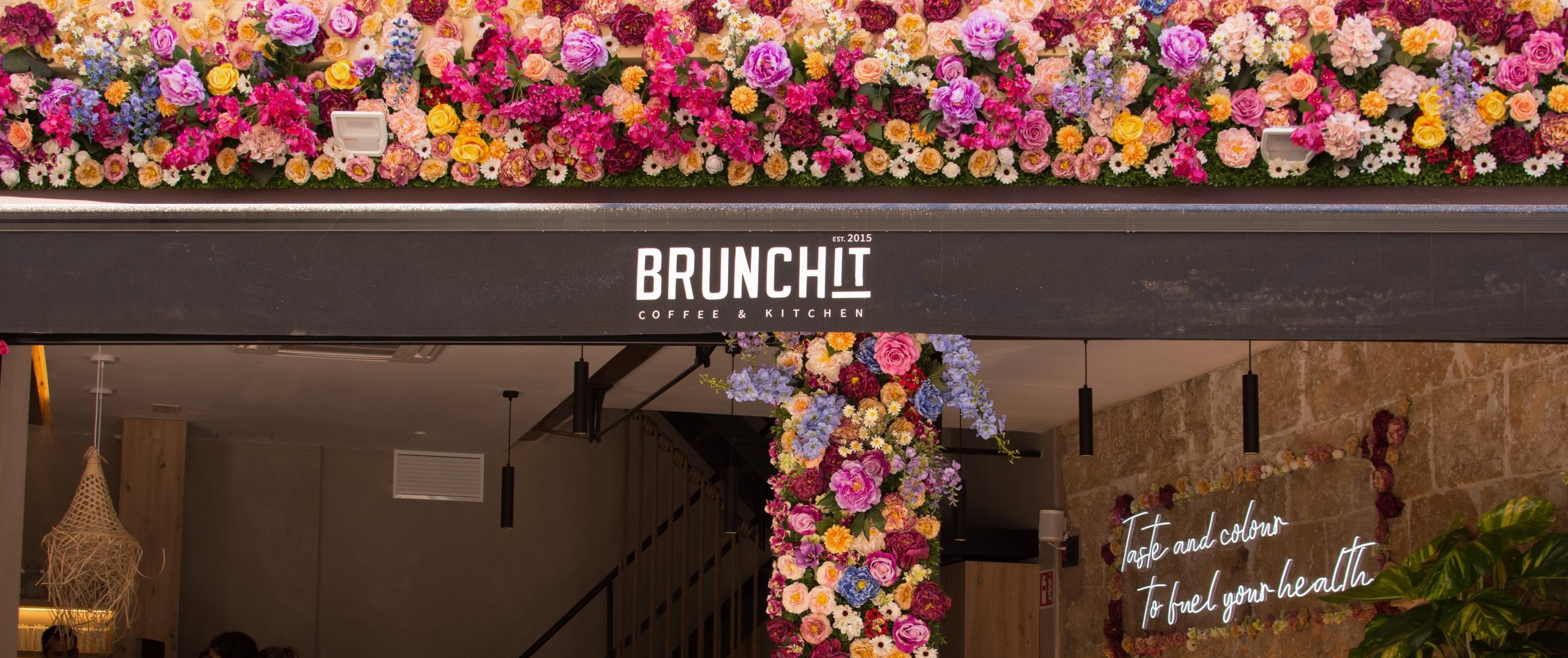 De ingang van BrunchIT met bloemenzuil, het uithangbord en de neonletters binnen