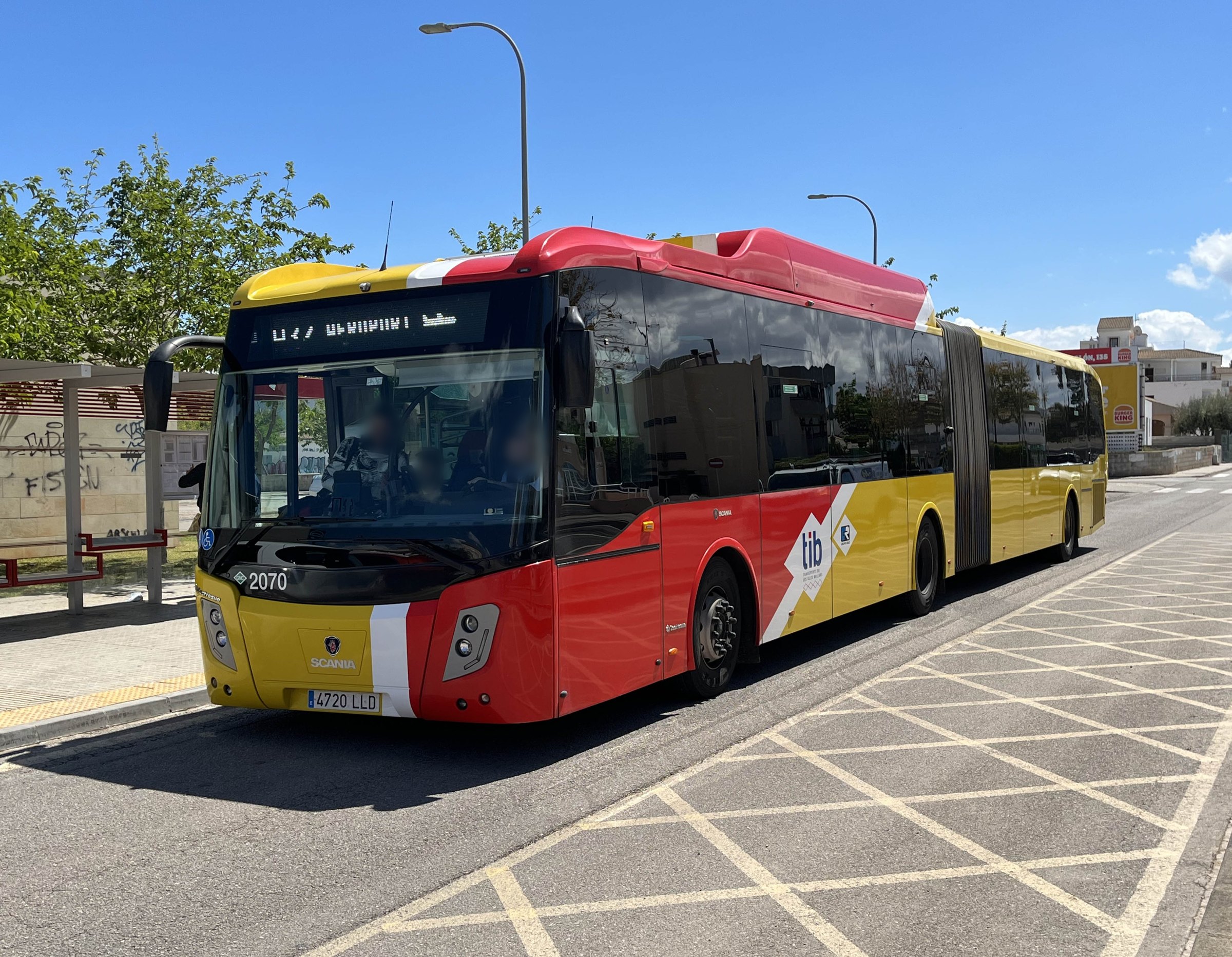 Gele en rode gelede TIB-bus met bestemming Aeroport bij een bushalte op Mallorca