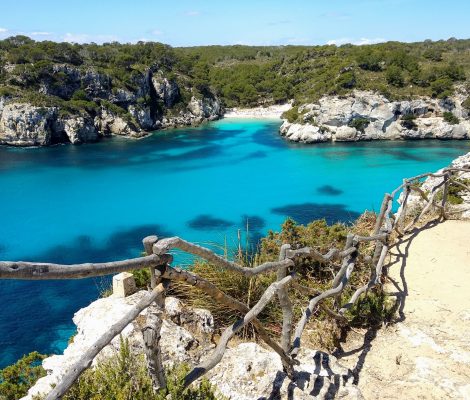 Turquoise baai van Cala Macarella op Menorca, gezien vanaf het kustpad met een houten reling