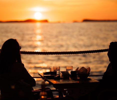 Twee gasten als silhouet aan een tafel op het terras van Café del Mar, met de zon die boven zee ondergaat