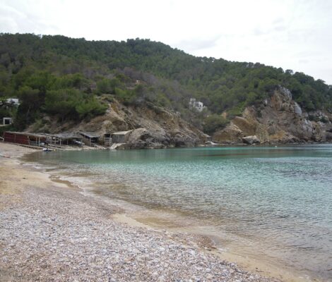 De baai van Cala Benirràs op Ibiza met helder water, de boothuisjes en de beboste heuvels