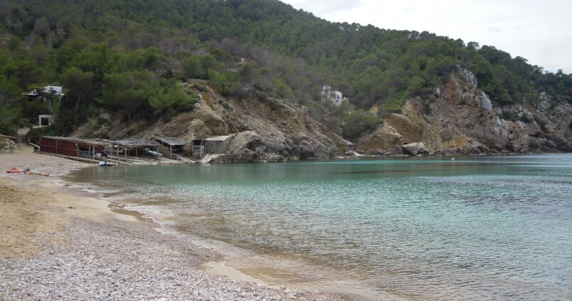 De baai van Cala Benirràs op Ibiza met helder water, de boothuisjes en de beboste heuvels