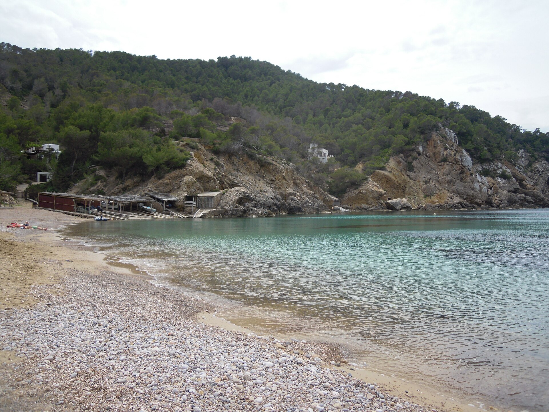 De baai van Cala Benirràs op Ibiza met helder water, de boothuisjes en de beboste heuvels