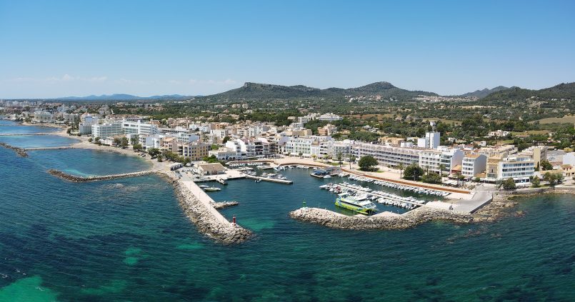 Luchtfoto van de haven van Cala Bona op Mallorca met turquoise water, de havenhoofden, de witte bebouwing en de groene heuvels erachter