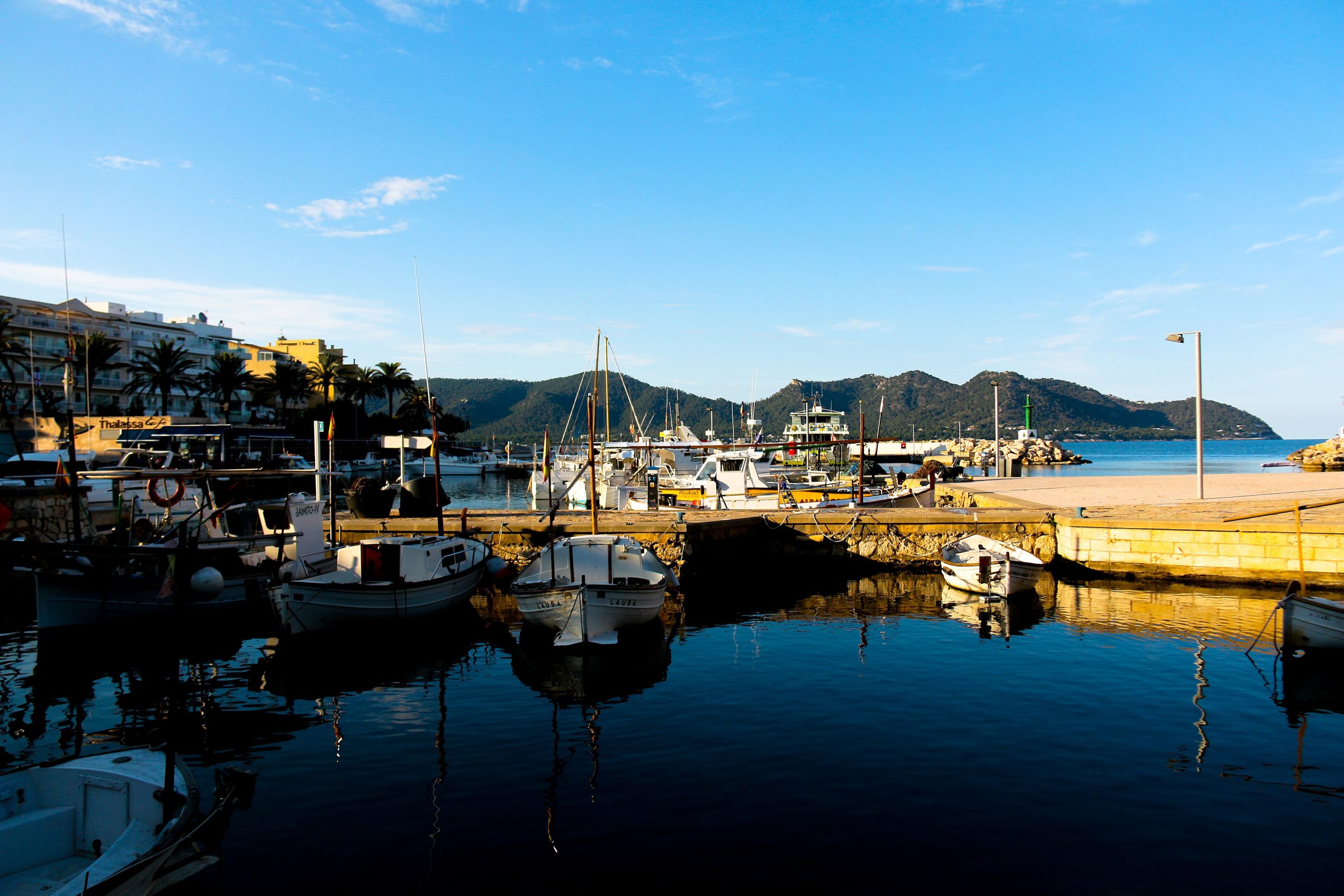 De havenkom van Cala Bona met afgemeerde vissers- en plezierboten, blauwe lucht en de bergen op de achtergrond