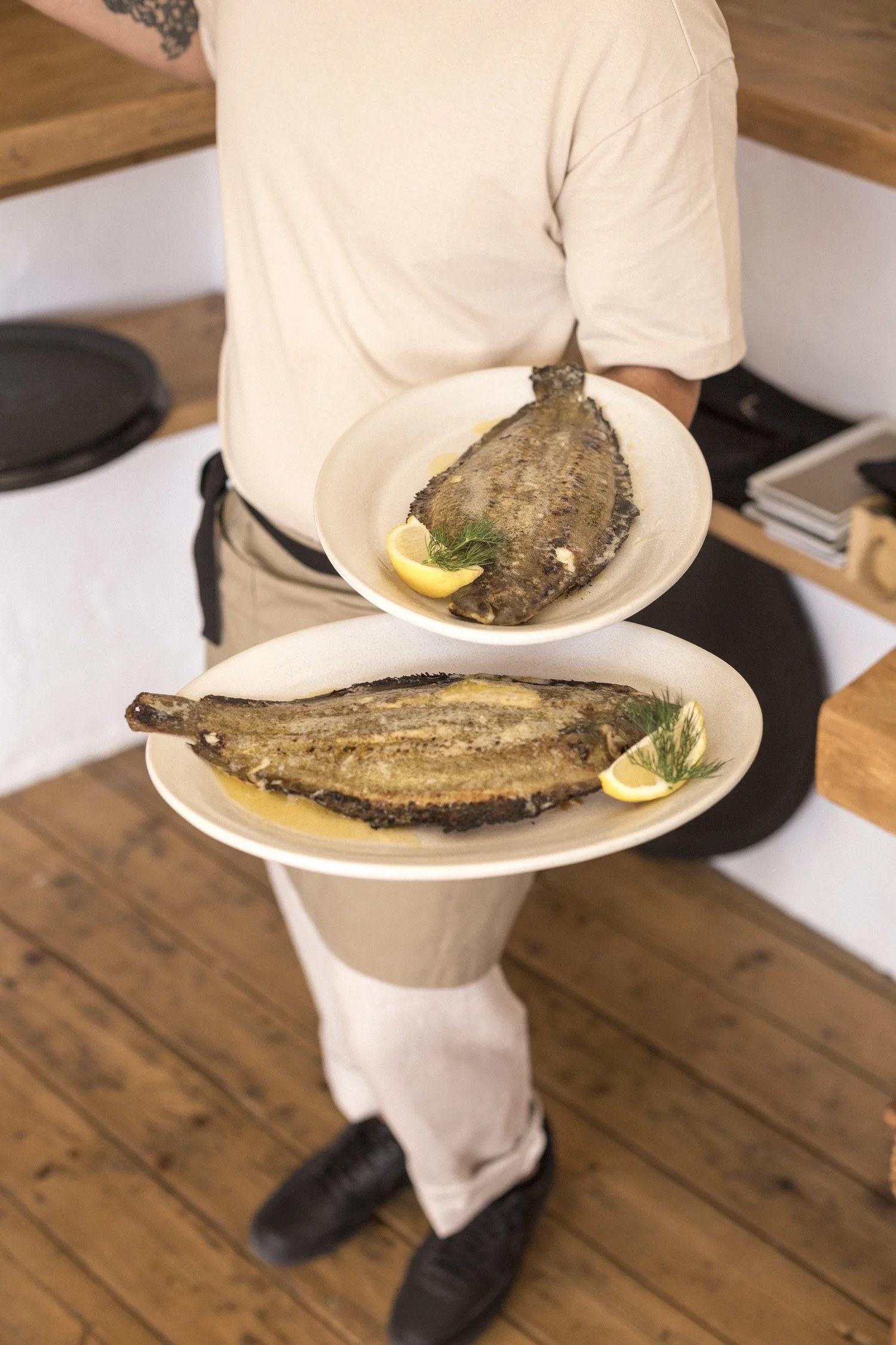 Een ober draagt twee borden met hele gegrilde vis bij Cala Bonita