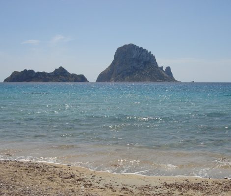 Het zandstrand van Cala d'Hort op Ibiza met helder water en de rotseilanden Es Vedranell en Es Vedrà aan de horizon