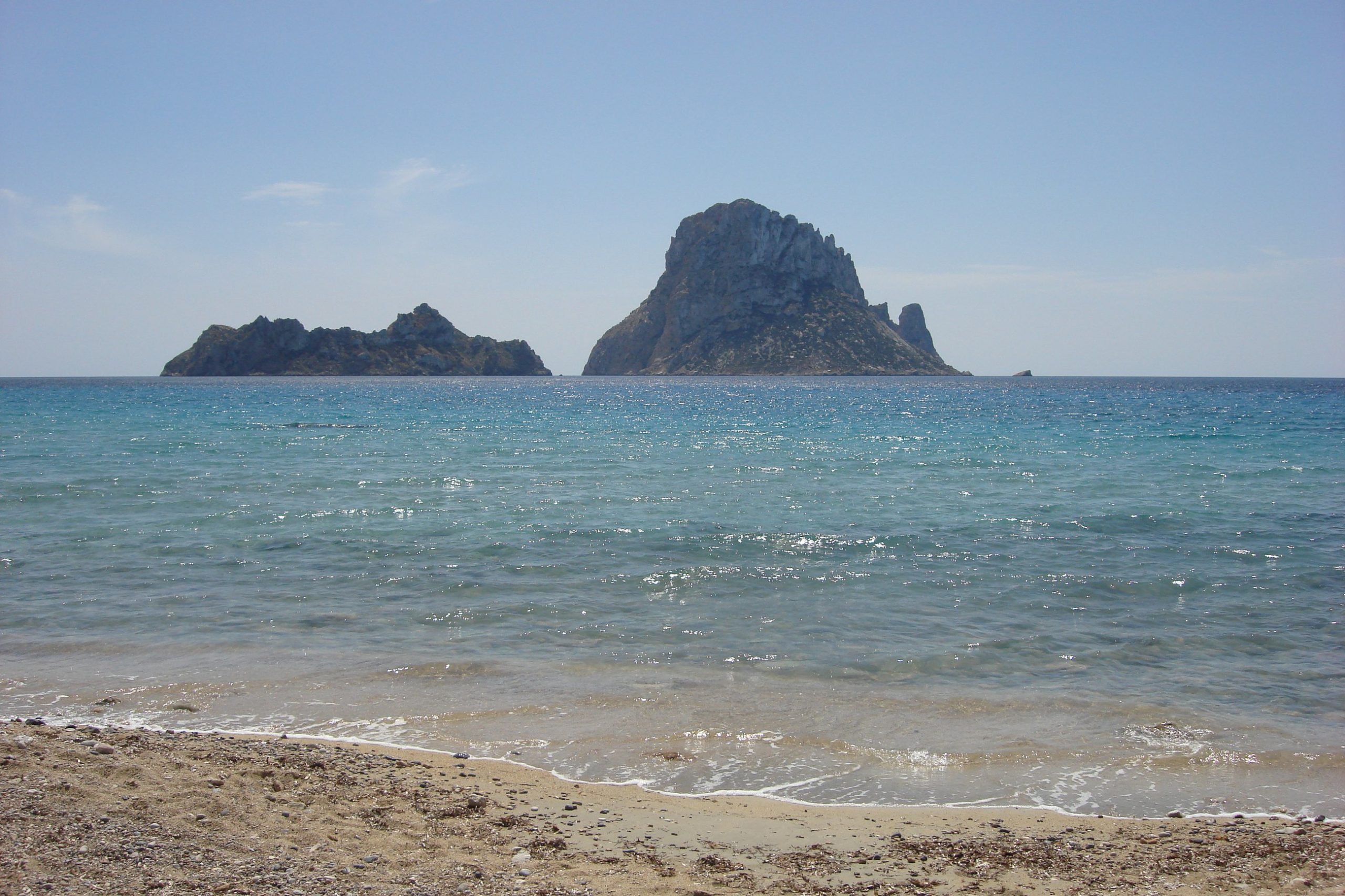 Het zandstrand van Cala d'Hort met helder water en de rotseilanden Es Vedranell en Es Vedrà aan de horizon
