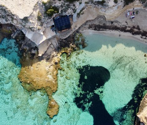Luchtfoto van Cala Escondida (es Racó d'en Xic) bij Cala Comte op Ibiza, met een strookje zand, turquoise water en zeegras